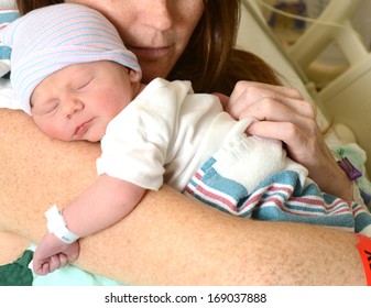 New Mother Holding A Sleeping Newborn Infant In Hospital