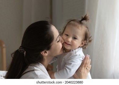 New mother lifting and holding little kid in arms, kissing baby with love, tenderness, affection. Mom cuddling sweet toddler, enjoying motherhood, maternity leave, care of baby girl
