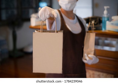 New normal An asian woman wearing gloves and medical face masks delivering take away food bags to customers at the restaurant bar to prevent the spread of corona virus.takeaway concept. space for logo
