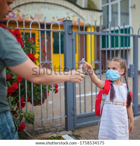 New normal back to school. Middle-aged father passing her daughter who waking to school in medical mask a sanitizer. Stay safe, social distance line on the ground
