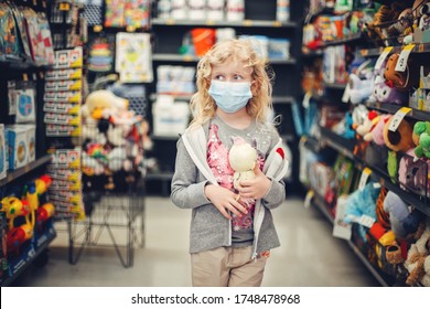 A New Normal. Caucasian Blonde Girl In Sanitary Face Mask Shopping At Toy Store. Child Wearing Protective Mask Against Coronavirus. Safety, Health Protection During Covid-19 Quarantine. 