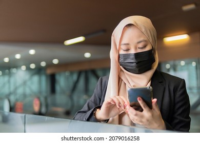 New Normal Concept: Young Malay Lady Wearing Face Mask Holding Smartphone