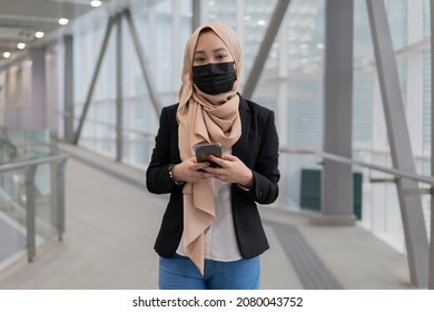 New Normal Concept: Young Malay Lady Wearing Face Mask Holding Smartphone