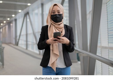 New Normal Concept: Young Malay Lady Wearing Face Mask Holding Smartphone