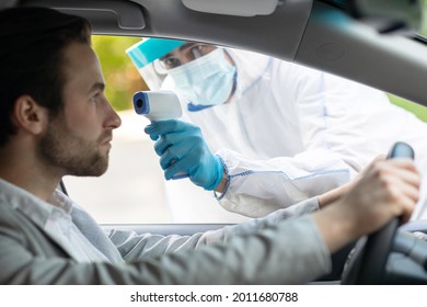 New Normal, Control, World Pandemic, Covid-19 On Road In Transit. Medical Worker In Hazmat Suit Measuring Temperature Of Young Male Driver At Wheel, Through Car Window Before Leaving Quarantine Zone