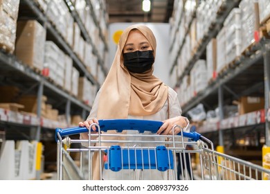 New Normal Retail Shopping: Cute Malay Girl Wearing Headscarf And Mask At The Store Holding Trolley