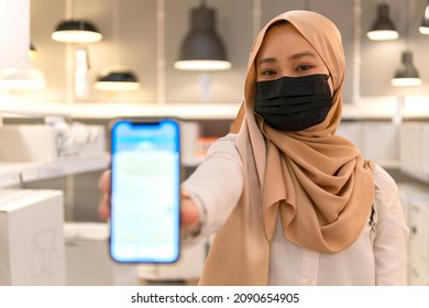 New normal retail shopping: Cute Malay girl wearing headscarf and mask at the store showing vaccination certificate