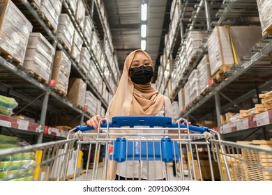 New normal retail shopping: Cute Malay girl wearing headscarf and mask at the store holding trolley
