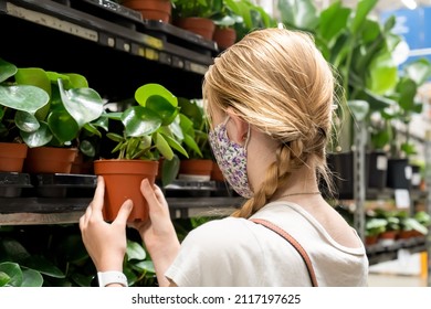 New Normal Retail Shopping. A Girl Wearing Face Mask Choosing Potted Plants In Retail Garden Warehouse Store. Covid-19 Pandemic