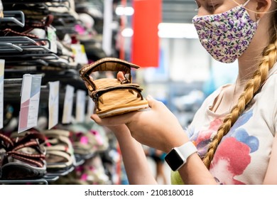 New normal retail shopping. Teenage blond girl wearing face mask choosing walking shoes sandalds at sport warehouse retail shop. Covid-19 pandemic