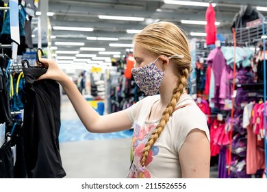 New normal retail shopping. Teenage blond girl wearing face mask choosing sports clothing at sport warehouse retail shop. Covid-19 pandemic
