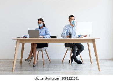 New Normal Rules. Diverse Female And Male Colleagues In Disposable Face Masks Working Together Using Pc Sitting At Desk. Modern Workplace And Workspace. People Returning Back To Office After Lockdown