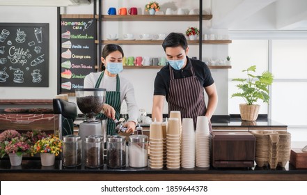 New Normal Startup Small Business Of Coffee Shop Concept. Male And Female Barista In Face Mask And Standing Behind Bar Counter In Cafe. Young Barista Wear Aprons And Check Customer Order For Delivery.