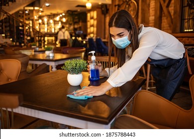 New Normal Startup Small Business Portrait Of  Woman Barista Wearing Protection Mask Cleaning Table In Coffee Shop While Social Distancing. New Normal Hygiene Restaurant Concept.