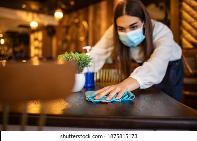 New Normal Startup Small Business Portrait Of  Woman Barista Wearing Protection Mask Cleaning Table In Coffee Shop While Social Distancing. New Normal Hygiene Restaurant Concept.