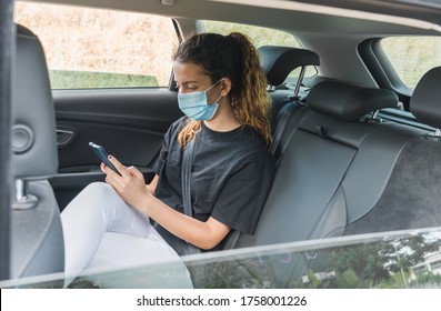 New normal. Teenager sitting in the back of a car with a mask. Young woman in a taxi protected by a mask. Safety and pandemic concept. Coronavirus devices. Social distance. Young girl using smartphone - Powered by Shutterstock