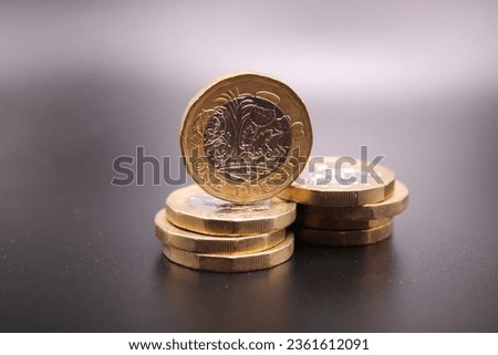 New one pound coins on a dark background.  Piles of coins and one standing on top of the other coins.  British coin.  British pound. Dark background.  Black background