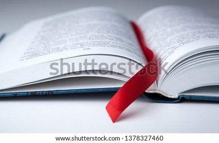 new open book on a gray table with a red ribbon bookmark close up