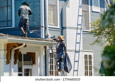 NEW ORLEANS, LA - JUNE 17, 2020: Spray Washer And Assistant Working On Roof Of House Prepping For Exterior Paint Job