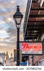 New Orleans, LA - October 28, 2021: A Neon Sign And Street Lamp On Bourbon Street With The City Skyline And Sunset Beyond, In The French Quarter.