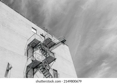 NEW ORLEANS, LA, USA - APRIL 19, 2022: Black And White Image Of A Fire Escape On The Side Of Tall Building And Wispy Clouds In The Background