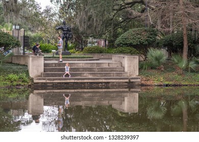 New Orleans, Louisiana / USA - February 16, 2019: A Young Girl's Reflection Shows In A Pond While She Relaxes In The Beautiful Sculpture Garden Outside The New Orleans Museum Of Art (NOMA).