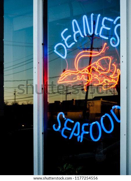 New Orleans, USA - Nov 28,\
2017: External lit up neon sign of Deanie\'s Seafood Restaurant as\
viewed from an outside window. Reflections of the car park area at\
dusk.