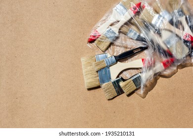 The New Paint Brushes Spilled Out Of The Plastic Bag Onto The Table. Hardboard Background. Top View.