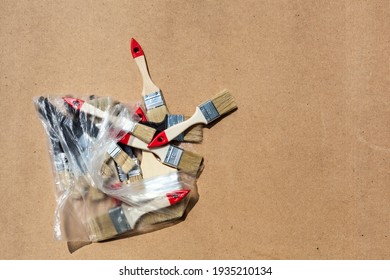 The New Paint Brushes Spilled Out Of The Plastic Bag Onto The Table. Hardboard Background. Top View.