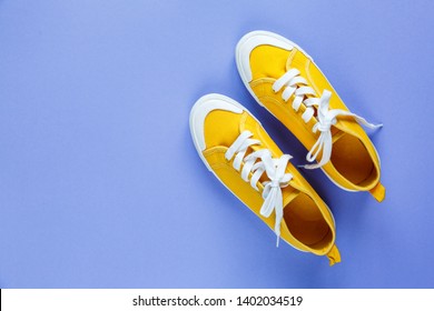 New pair of yellow sneakers on violet background with copy space. Lifestyle  sneaker sport shoe. 