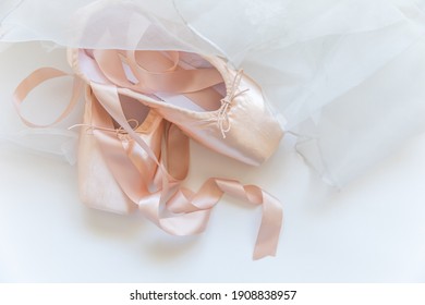 New pastel beige ballet shoes with satin ribbon and tutut skirt isolated on white background. Ballerina classical pointe shoes for dance training. Ballet school concept. Top view flat lay copy space