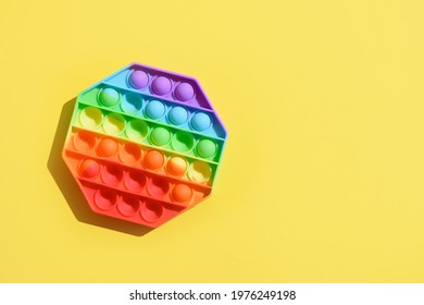 New popular silicone colorful antistress pop it toy for child on yellow background. View from above. Copy space. Simple dimple