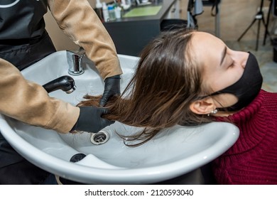 In The New Prestigious Salon, A Master In Special Gloves Prepares A Client To Wash Her Head In A Special Chair During An Epidemic. Hairdressing Concept. Beauty Salon Concept