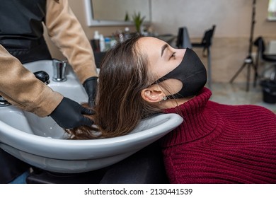 In The New Prestigious Salon, A Master In Special Gloves Prepares A Client To Wash Her Head In A Special Chair During An Epidemic. Hairdressing Concept. Beauty Salon Concept