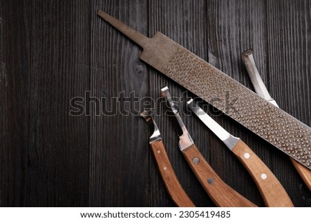 new professional hoof knives with  rasp for trimming horsy foot against black wooden background. horse hoof care concept