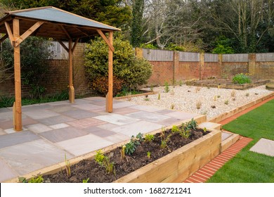 A New Raised Patio With A Wooden Gazebo In Front Of A Raised Flowerbed And A Gravel Garden Area.