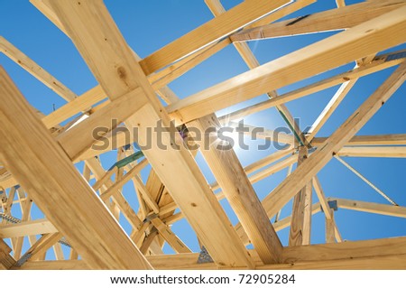 New residential construction home framing against a blue sky and sun