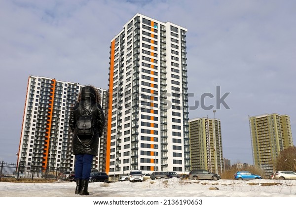 New residential district in\
city, woman in black leather coat standing on apartment buildings\
background. Real estate, choosing home or renting property\
concept