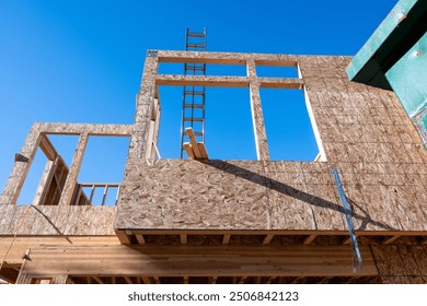 New residential home construction in framing stage, looking up at second floor with OSB, oriented strand board, installed on exterior wall and aluminum extension ladder across window opening
 - Powered by Shutterstock