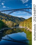 New River Gorge Bridge in the fall. The vertical photo taken from the bottom of the gorge shows the bridge reflected in the river with colorful autumn foliage on the mountainsides. Fayetteville, WV