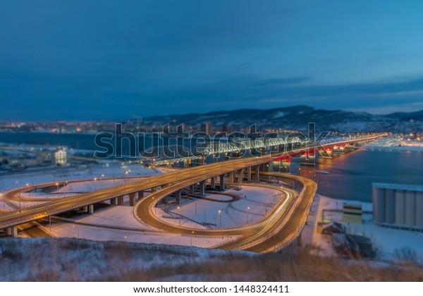 The new road bridge, illuminated by lanterns and\
moving cars, a beautiful reflection of the bridge in the Yenisei\
and the nearby railway bridge in the lights - a beautiful night\
landscape from above.