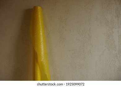 New Roll Of Yellow Vapor Barrier Near Stone Wall.