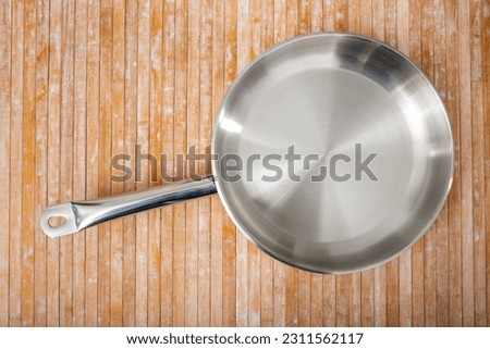 New shiny stainless steel frying pan on a wooden table. Close-up image..