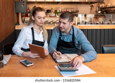 New small business owners counting revenue and expenses - Start-up entrepreneurs, woman and man, businessmen doing accounting with calculator and tablet in Restaurant