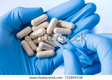 New small pill in tweezers in scientist hands, medicine research concept
