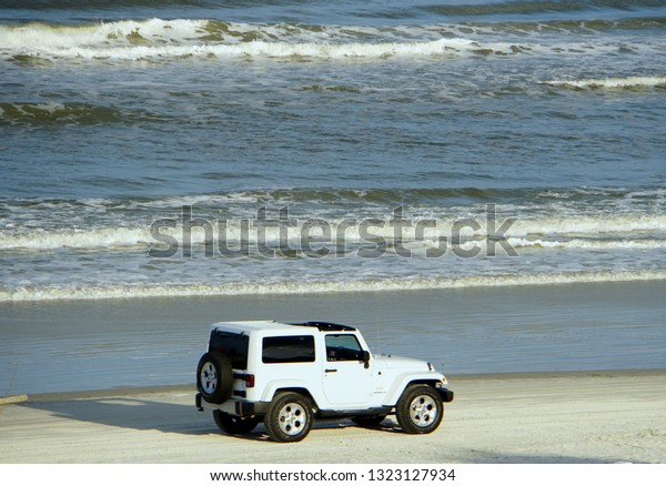 New Smyrna Beach, Florida,\
U.S.A - February 18, 2019 - A white Jeep Wrangler moving on the\
beach