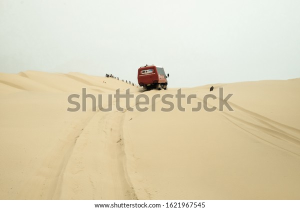 New South Wales, Australia\
- December 30, 2019: A red off-road truck driving in the desert or\
sand dunes near Port Stephens, picking-up the tourists to the upper\
zone
