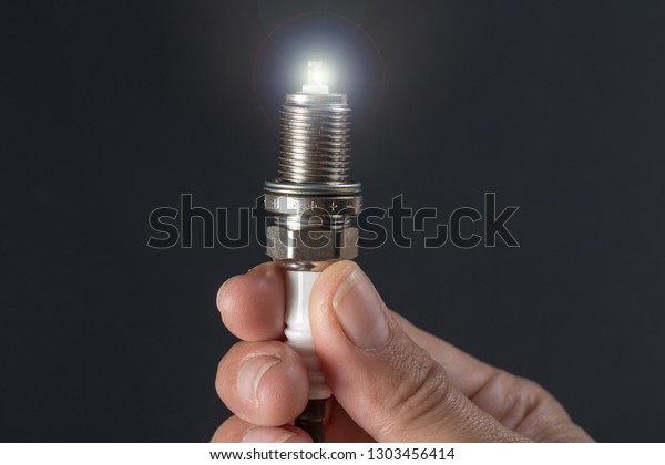New spark plug in\
hand on a dark background