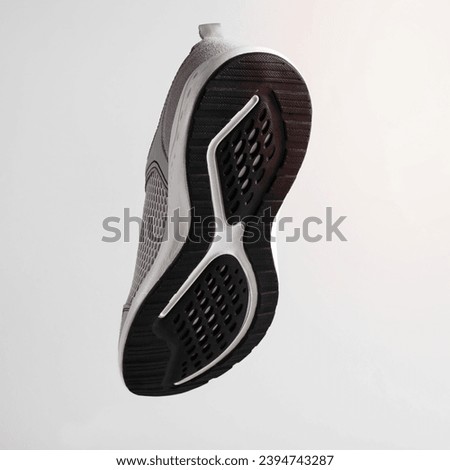New sports shoes with textured black sole, levitation on light background. Close-up of sneaker flying in air, back view.