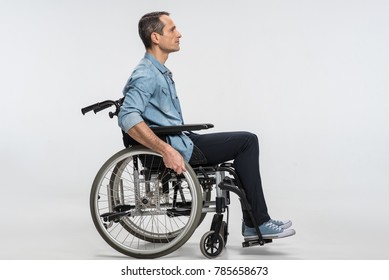 New start. Thoughtful concentrated handicapped man touching wheels and sitting in profile while moving ahead  - Powered by Shutterstock